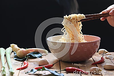 Woman hand holding chopsticks of instant noodles in cup with smoke rising and garlic on dark background, Sodium diet high risk Stock Photo