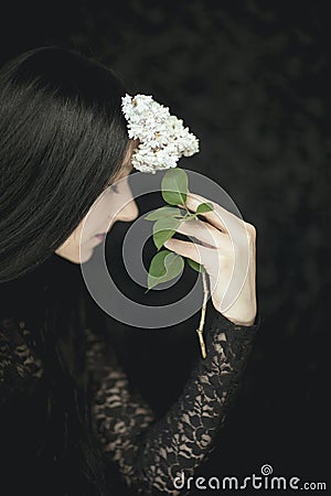 Woman hand holding fresh white lilac flowers to her face, very dark atmospheric sensual rural studio shot Stock Photo