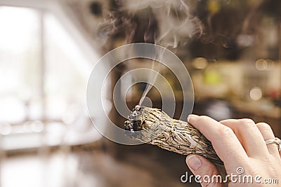 Woman hand holding herb bundle of dried sage smudge stick smoking. Stock Photo