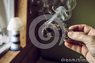 Woman hand holding herb bundle of dried sage smudge stick smoking. Stock Photo