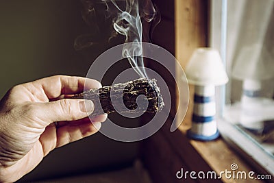 Woman hand holding herb bundle of dried sage smudge stick smoking. Stock Photo