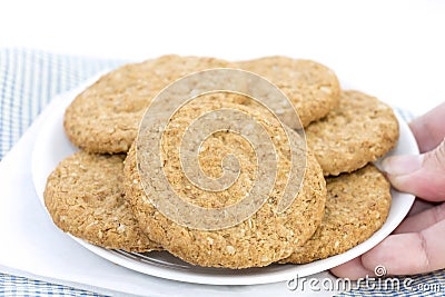 Woman hand holding homemade shortbread cookies made of oatmeal pile in plate on blue cloth background. Concept food healthy snack Stock Photo