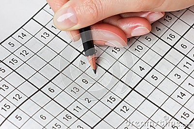 Woman hand holding a pencil and solves crossword sudoku Stock Photo