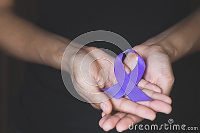 Woman Hand Holding Purple Ribbon, Domestic Violence Awareness Month October concept with deep purple awareness ribbon Stock Photo