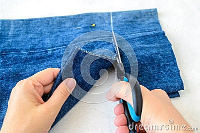 Woman hand holding a scissors and cutting out a folded in half blue jean shorts. Shorten the denim shorts with scissors and sewing Stock Photo