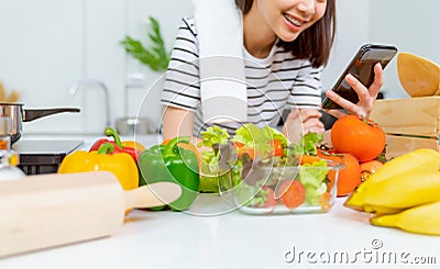 Woman hand holding a smartphone and salad bowl with tomato and various green leafy vegetables. Stock Photo