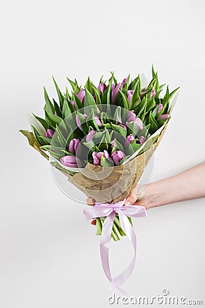 Woman hand holding soft lilac tulips flowers on white background. bouquet decorated with kraft paper Stock Photo