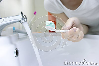 Woman hand holding toothbrush with toothpaste applied on it in bathroom. Close up of female hand ready for brushing teeth. Stock Photo