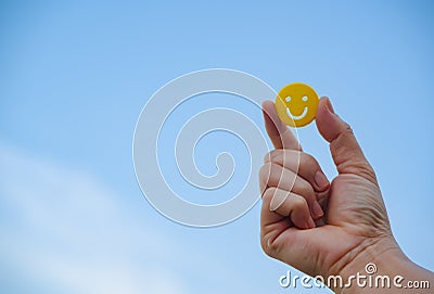 woman hand holding yellow emoticon smiley face icon symbol on blue sky background Stock Photo