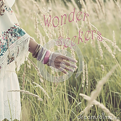 Woman hand with lot of boho style braceletes touching grass , summer day in the field with quote wonder seekers Stock Photo