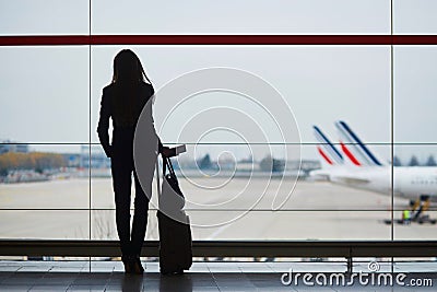 Woman with hand luggage in international airport, looking through the window at planes Stock Photo