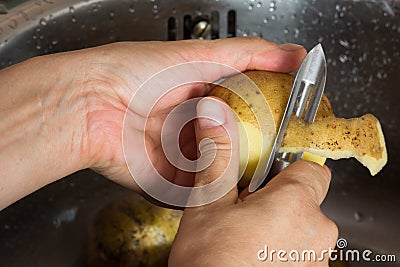 Woman hand peeling potato in the sink with peeler knife Stock Photo