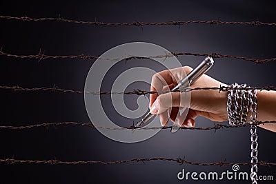 Woman hand with pen tied with chain and rusty sharp bare wire, depicting the idea of freedom of the press or expression. World Stock Photo