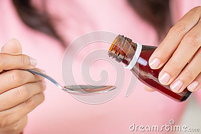 Woman hand pouring medication or antipyretic syrup from bottle to spoon. Stock Photo