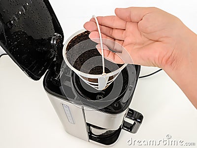 Woman hand removing mesh basket filter full of used ground coffee from drip-type coffee maker. Home electrical appliances. Stock Photo