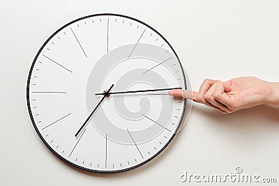 Woman hand stop time on round clock, female finger takes the minute arrow of the clock back, time management and deadline concept Stock Photo