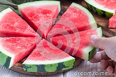 Woman hand take slice of fresh seedless watermelon cut into triangle shape laying on a wooden plate, horizontal Stock Photo