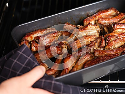 A woman hand taking a black baking tray with baked pork ribs out of an oven Stock Photo