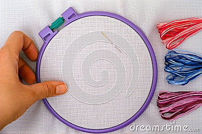 Woman hand taking plastic embroidery hoop with cross stitch fabric and some colour threads near Stock Photo