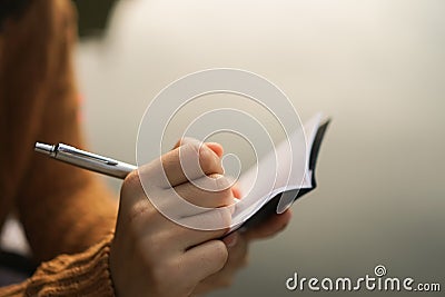 Woman hand writing down in small white memo notebook. Stock Photo