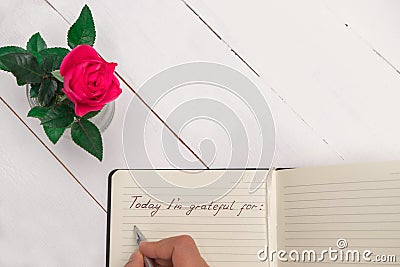 Woman hand writing in a gratitude journal on white wooden table background with pink rose decoration Stock Photo