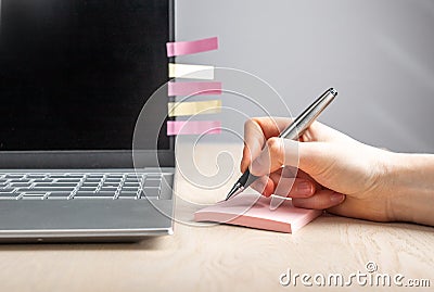 Woman hand writing reminders at sticky notes. Female sitting at desk with laptop and recording with pen key words and Stock Photo