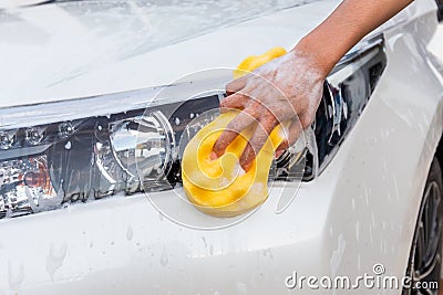 Woman hand with yellow sponge washing headlight modern car or cleaning automobile. Stock Photo