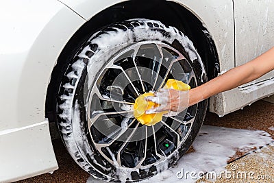 Woman hand with yellow sponge washing wheel modern car or cleaning automobile. Stock Photo
