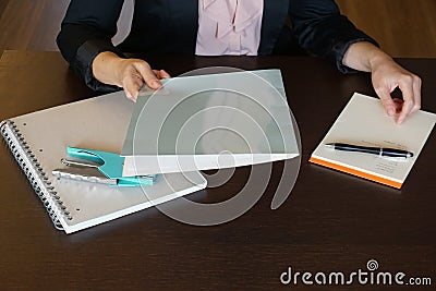 Woman is handing over a white file in direction camera while sitting at the desk in the office. Stock Photo