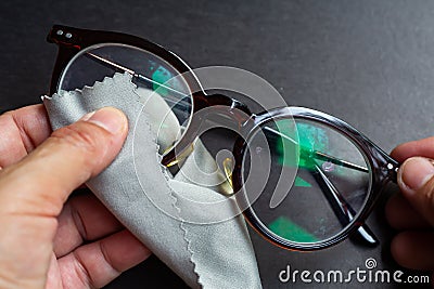 Woman hands cleaning shortsighted or nearsighted eyeglasses by microfibre cleaning cloths, On black background, Optical concept Stock Photo