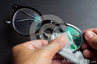 Woman hands cleaning shortsighted or nearsighted eyeglasses by microfibre cleaning cloths, On black background, Optical concept Stock Photo