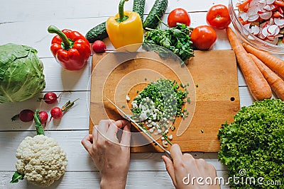 Woman hands cutting fresh green onion on wooden board overhead top view. White table background. Healthy cooking concept. Stock Photo