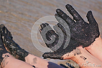 Woman hands and feet covered with black healing mud, sandy seashore in background Stock Photo