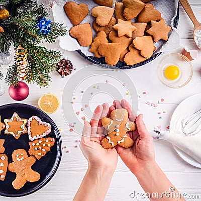 Woman hands holding traditional christmas gingerbread man cookies. White wooden table with ingrediens and decoration details. Chri Stock Photo