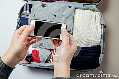 Woman hands with phone on the background of Open suitcase packed Stock Photo