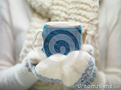 Woman hands in white and blue mittens holding a cozy knitted cup with hot cocoa, tea or coffee. Winter and Christmas time concept. Stock Photo