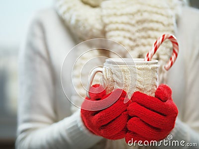 Woman hands in woolen red gloves holding a cozy mug with hot cocoa, tea or coffee and a candy cane. Winter, Christmas time concept Stock Photo