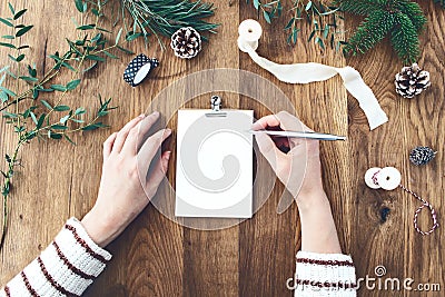 Woman hands writting Christmas wish list, goals, resolutions on empty letter card. Old oak wooden table with Christmas Stock Photo