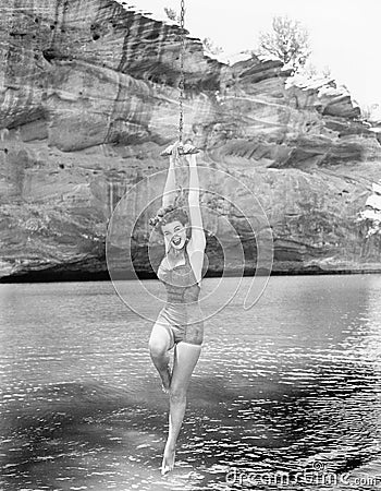 Woman hanging from rope swing over water Stock Photo