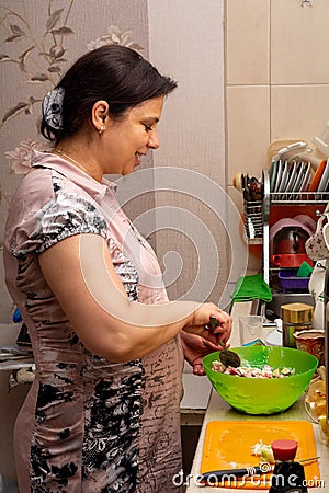 A woman happily prepares a salad in her kitchen. Healthy eating Stock Photo