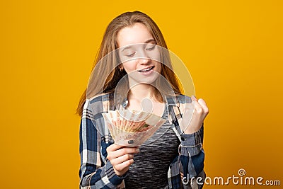 Woman, happy smiling, holding Russian rubles, wearing a plaid shirt, received a scholarship, a salary on a yellow background. Stock Photo