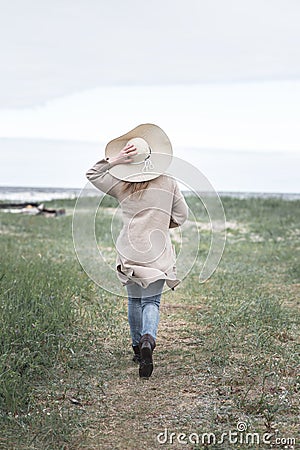 A woman in a hat and a long cardigan runs to the sea during a storm, rear view Stock Photo