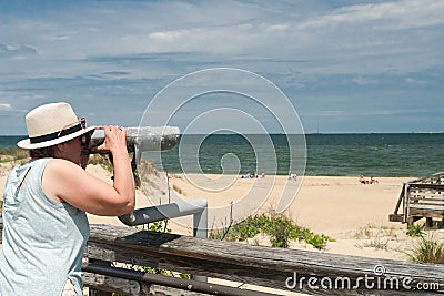 Woman in hat looks through Coin binoculars at ocean Stock Photo