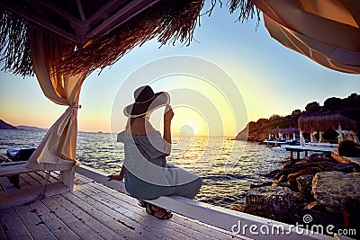 Woman in hat relaxing by the sea in a luxurious beachfront hotel resort at sunset enjoying perfect beach holiday vacation in Stock Photo