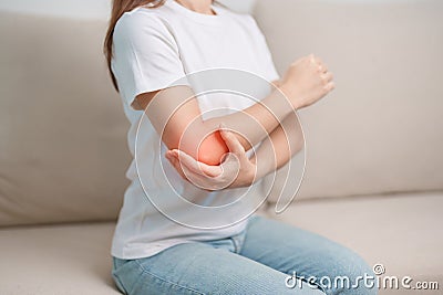 Woman having elbow ache during sitting on couch at home, muscle pain due to lateral epicondylitis or tennis elbow. injury, Health Stock Photo