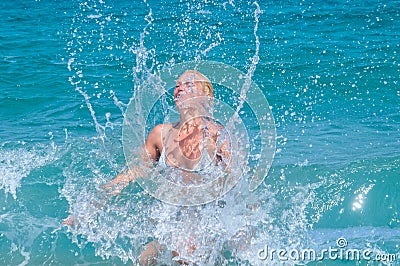 A woman having fun in the waves of the sea which are splashing her. The beautiful woman mother of three in bikini Stock Photo