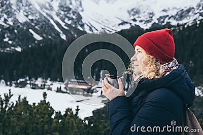 Woman having a hot drink from thermo cup overlooking snowcapped High Tatra mountains peaks Stock Photo
