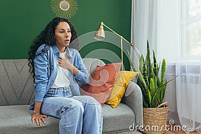 Woman having panic attack, Hispanic woman with curly hair alone at home depressed, having trouble breathing sitting on Stock Photo