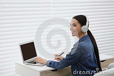 Woman in headphones studying on laptop indoors. Online translation course Stock Photo