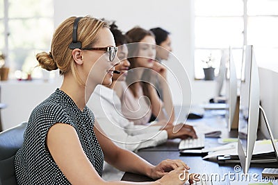 Woman with headset at computer in office beside colleagues Stock Photo